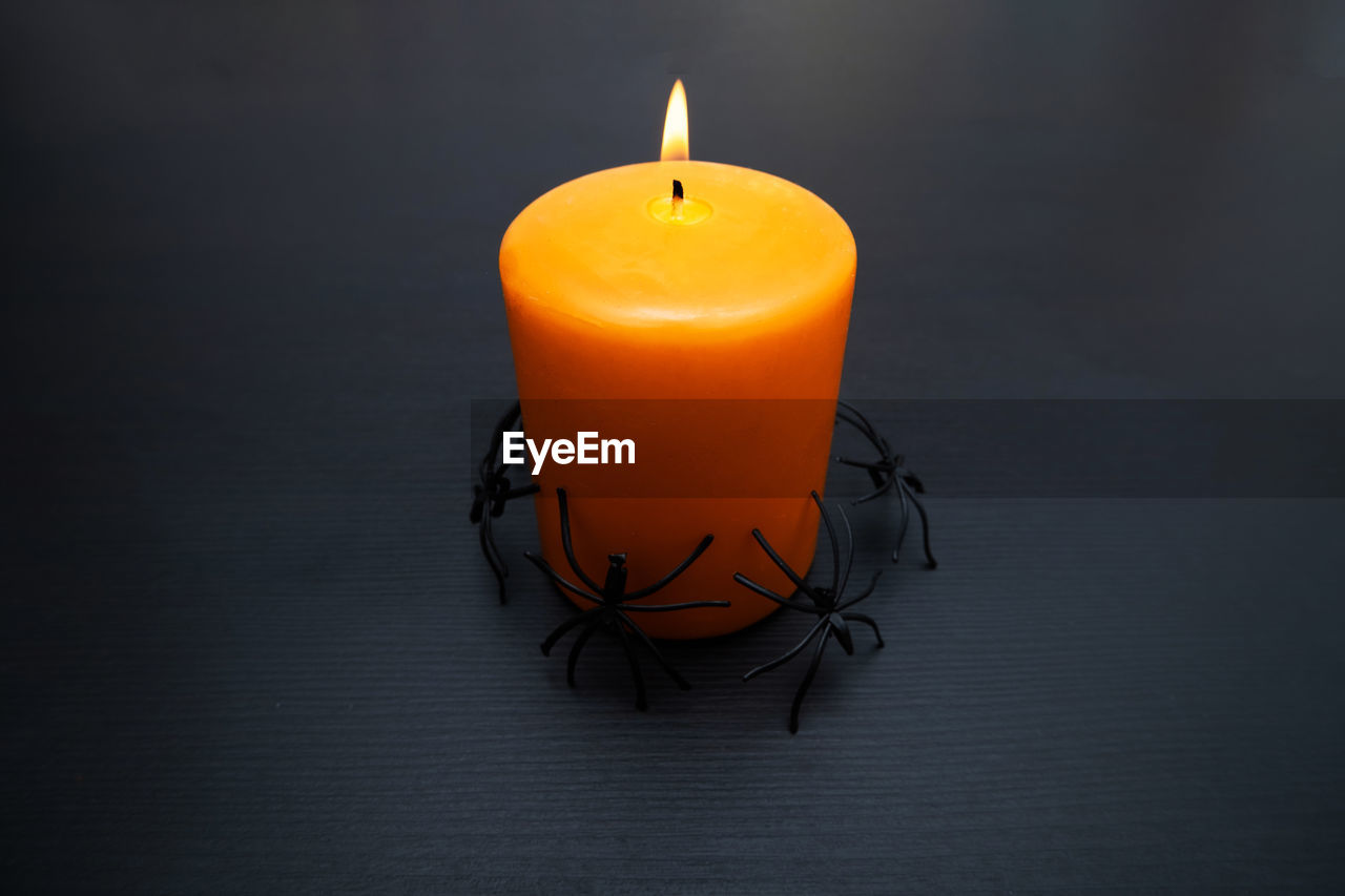 View of burning orange candle with spider around for halloween party with copy space.