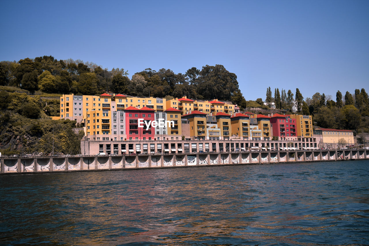 Scenic view of river by buildings against clear blue sky