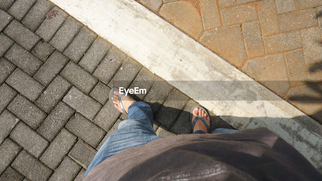 HIGH ANGLE VIEW OF MAN STANDING ON COBBLESTONE STREET