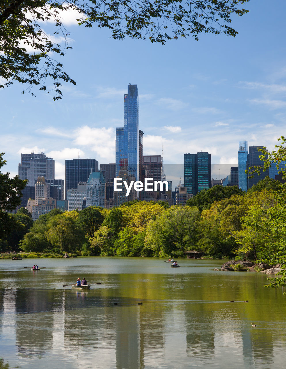 Scenic view of lake and trees against sky in city on sunny day at central park