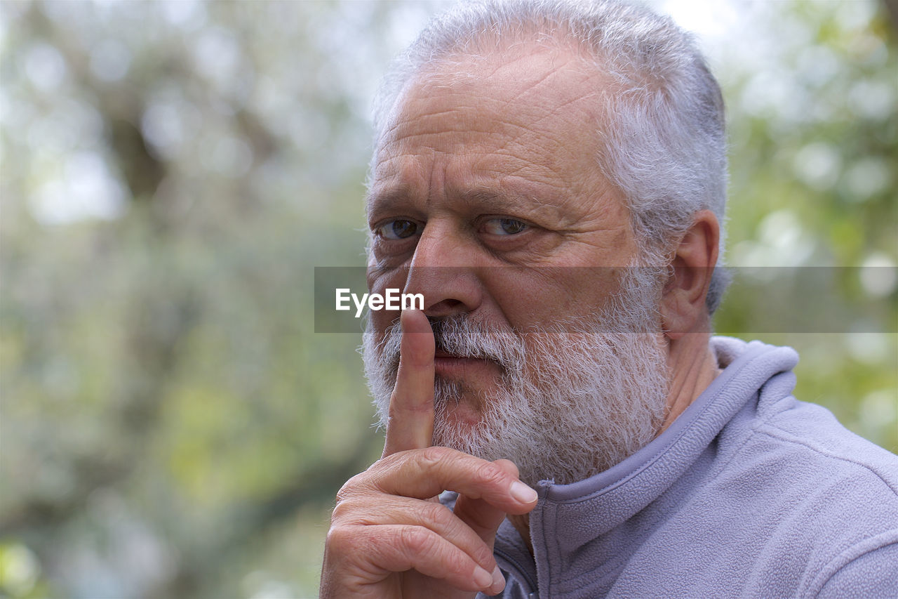 Close-up portrait of senior man with finger on lips