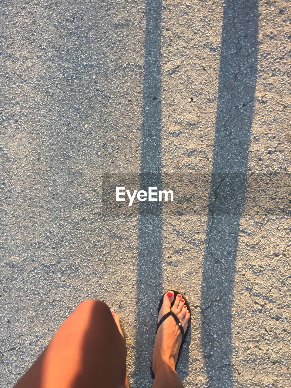 LOW SECTION OF WOMAN STANDING ON ROAD WITH SHADOW