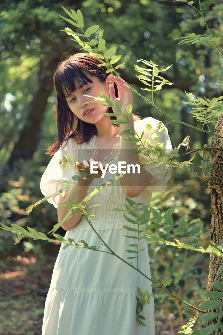 WOMAN STANDING BY PLANTS AGAINST TREES