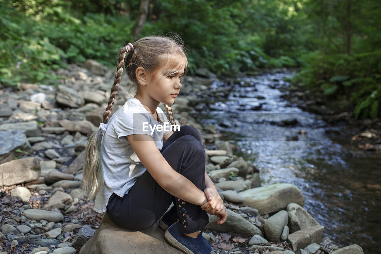 Full length of girl sitting on rock in forest