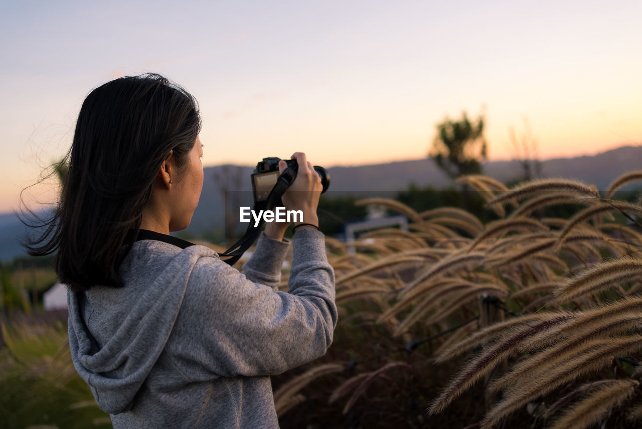 Mature asian woman using camera to shoot photos of flowers at sunset