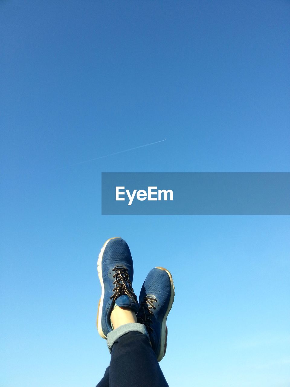 Low section of person with feet up against blue sky