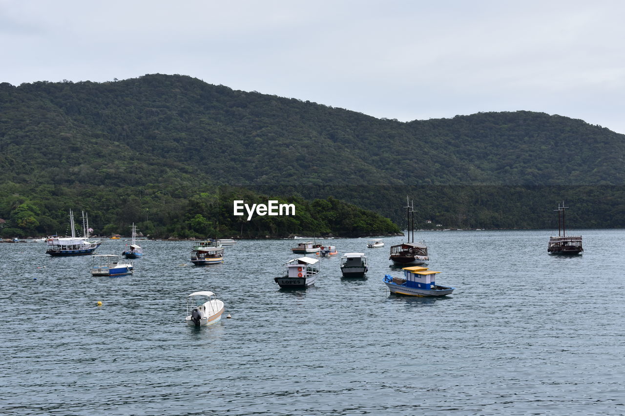 BOATS SAILING IN SEA AGAINST MOUNTAINS