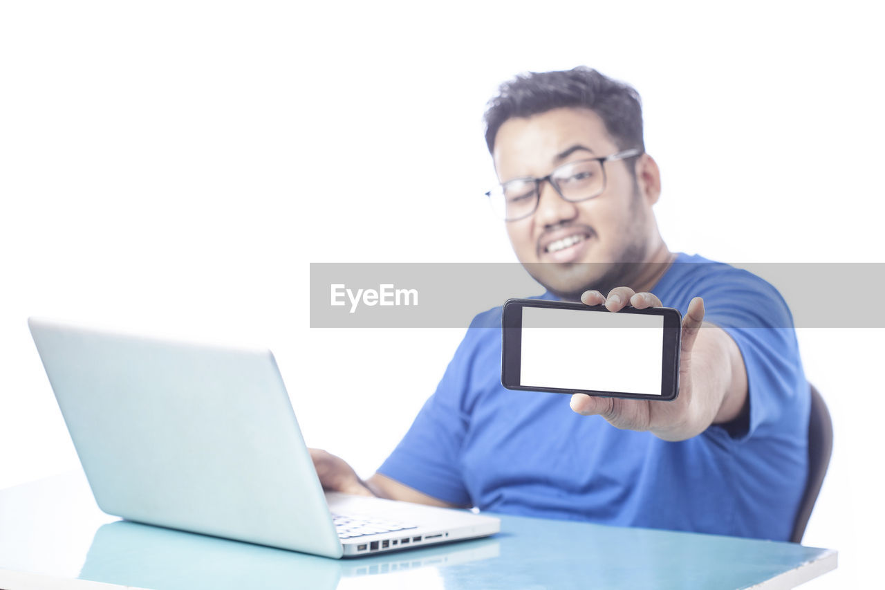 technology, wireless technology, computer, communication, laptop, one person, adult, using laptop, men, internet, smiling, eyeglasses, glasses, business, happiness, computer network, person, businessman, white background, e-mail, cheerful, indoors, portrait, portability, writing, front view, working, young adult, occupation, copy space, looking, computer equipment, emotion, studio shot, casual clothing, sitting, activity, furniture, black hair, table, using computer, desk, typing, learning, cut out, relaxation, office, waist up, holding, white-collar worker, button down shirt