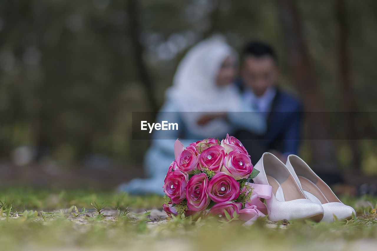 Close-up of rose bouquet and shoes against couple in park