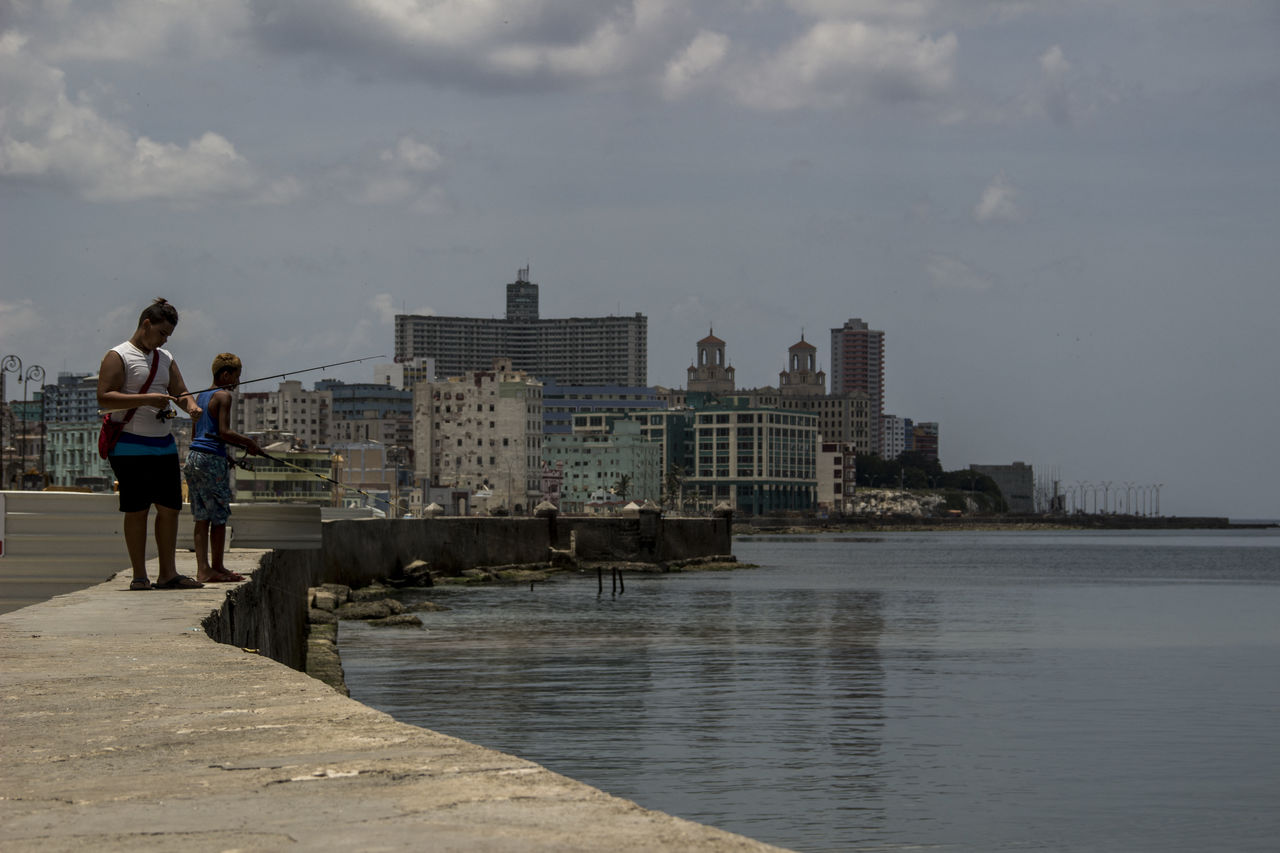 MAN STANDING BY SEA AGAINST SKY IN CITY