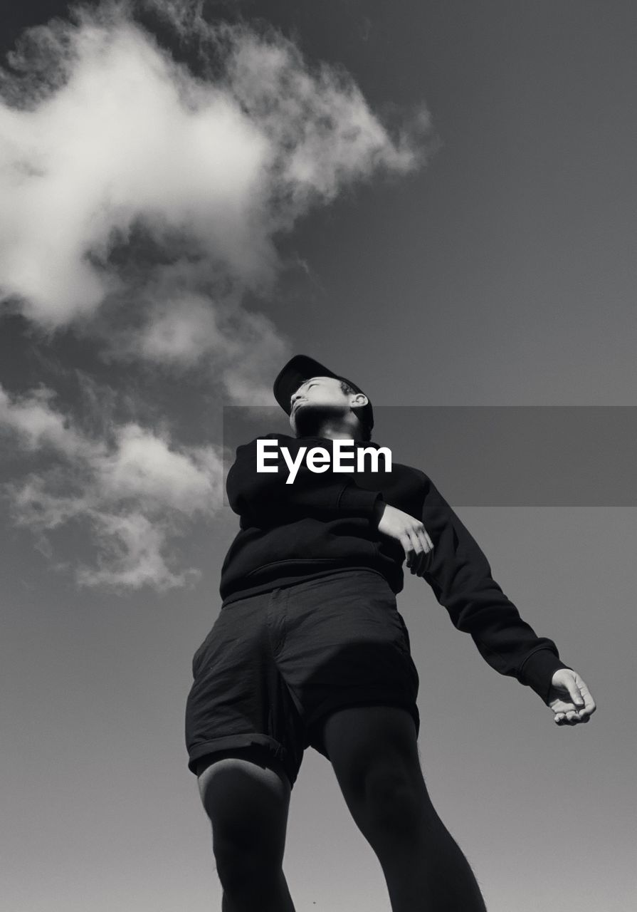 LOW ANGLE VIEW OF BOY STANDING AGAINST SKY