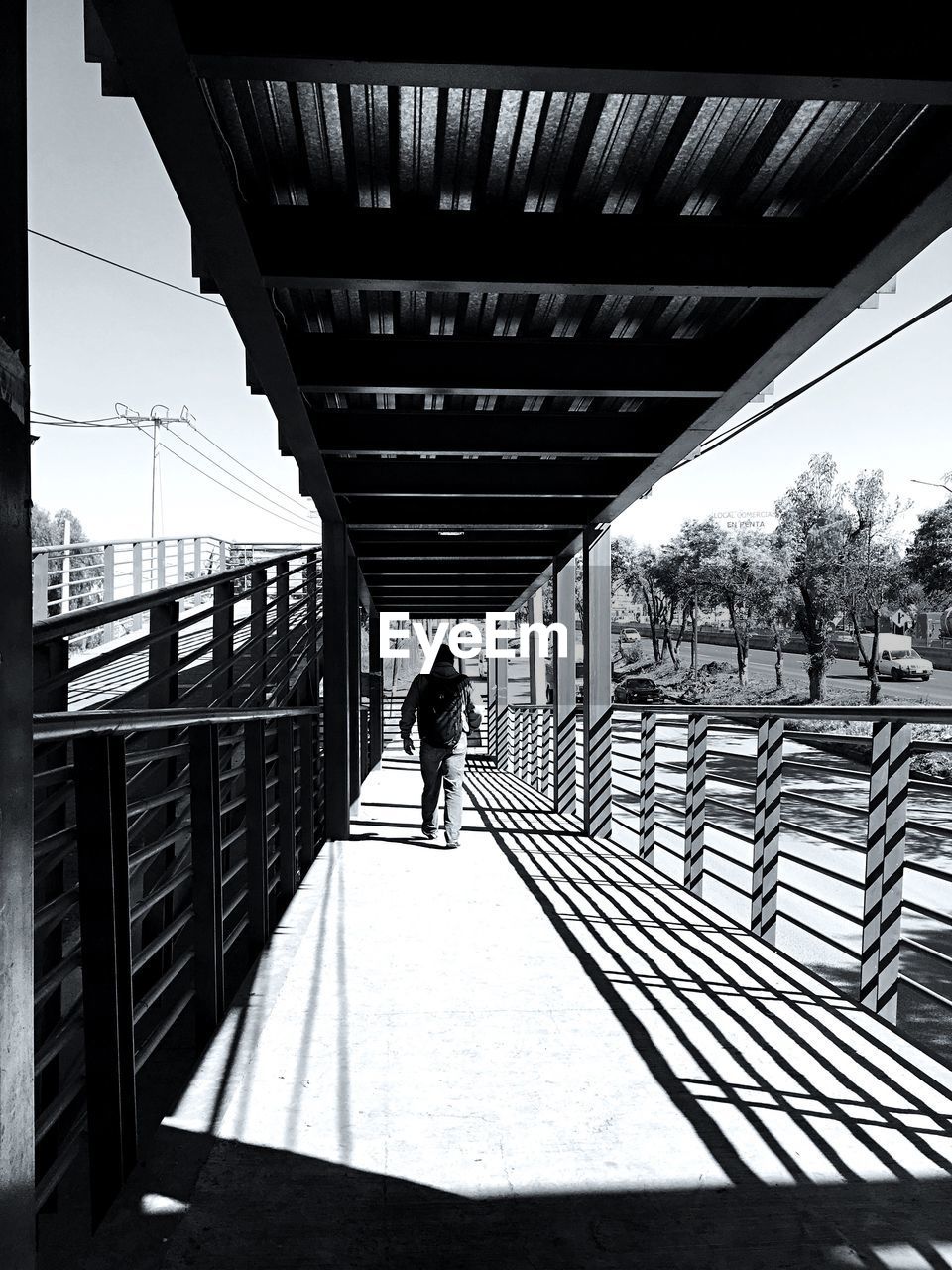 Rear view of man walking on footbridge at railway station during sunny day