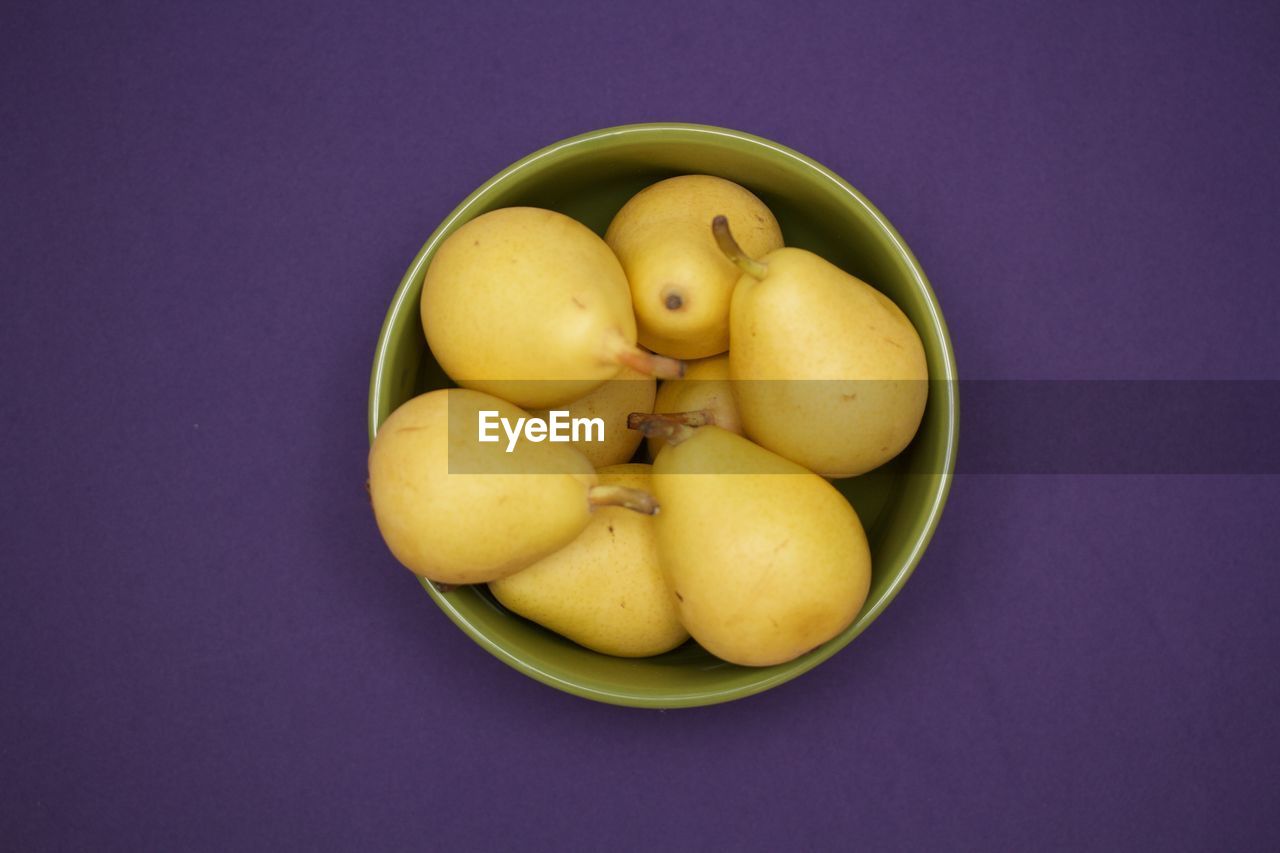 Pears in a green bowl on purple background