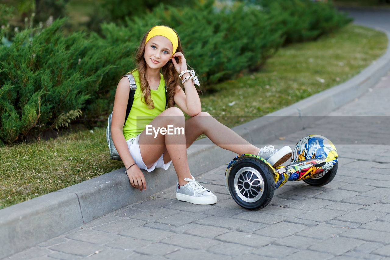 Full length portrait of teenage girl with hoverboard sitting at park