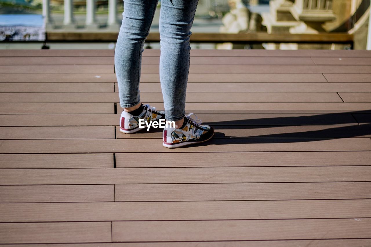 Low section of woman wearing shoes standing on boardwalk during sunny day