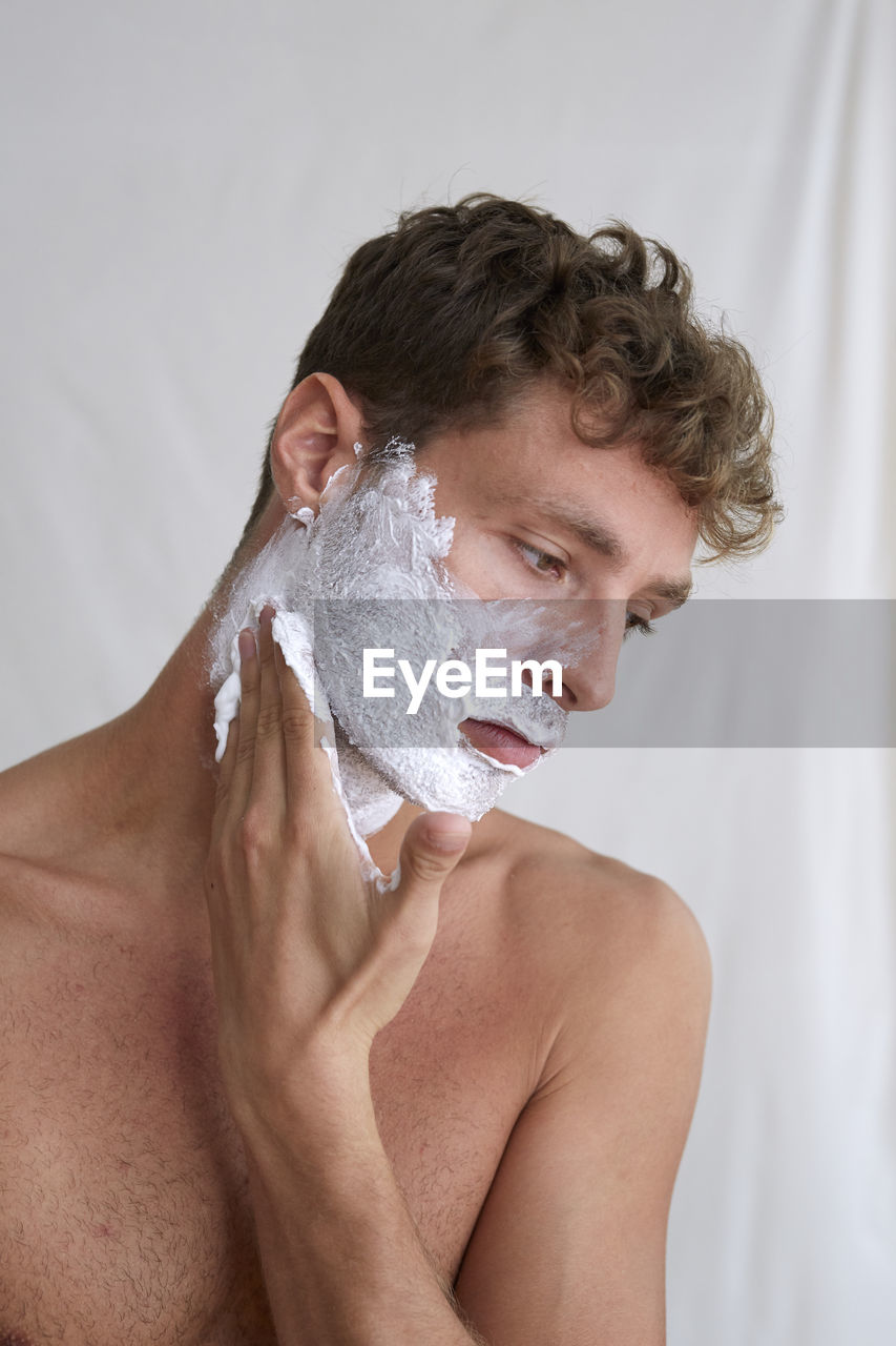 Close-up of young man applying shaving cream at home