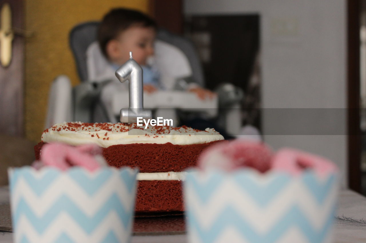 Close-up of cake with baby sitting at background
