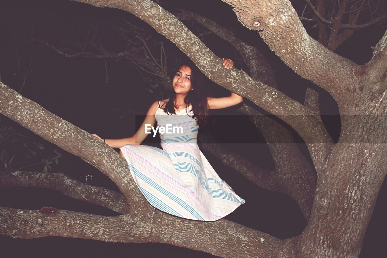 Portrait of young woman standing on tree at night