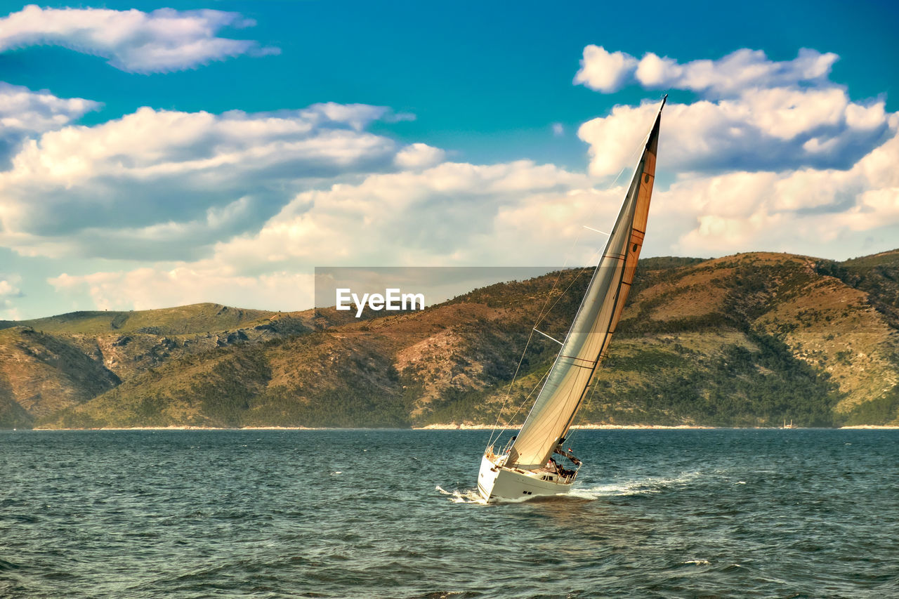 Boat sailing on sea by mountain against sky