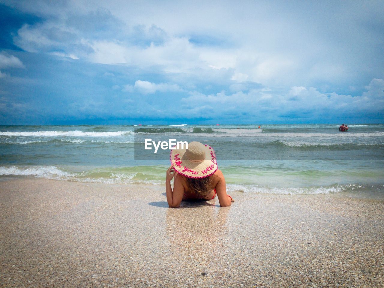 Woman wearing sun hat and lying on her back near the sea on a day with dark storm clouds