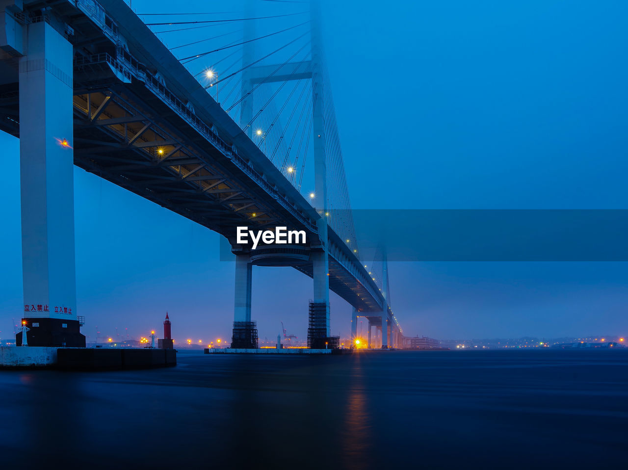 Illuminated bridge over bay in port of yokohama against sky at dawn on a foggy morning.