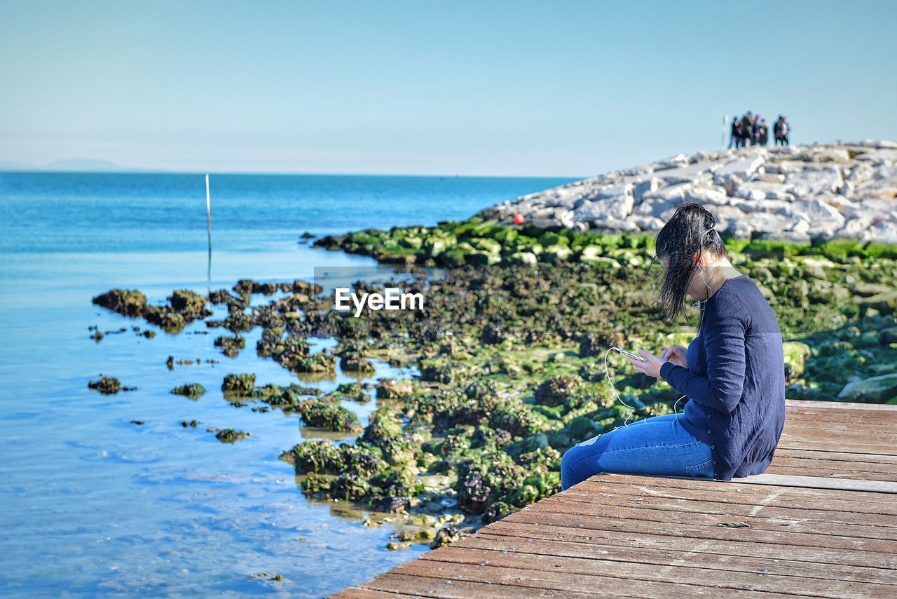 Side view of woman using smart phone while sitting on pier