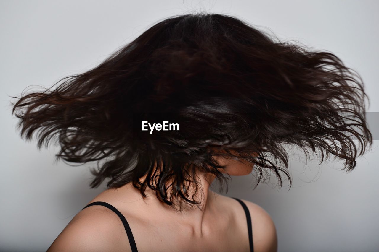 Close-up of woman tossing short hair against gray background