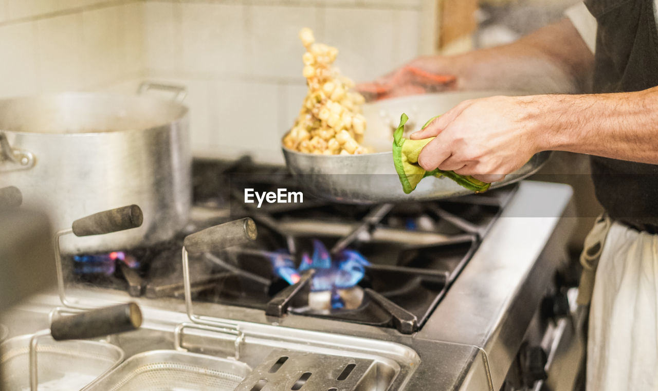 Midsection of chef keeping utensil on stove in kitchen