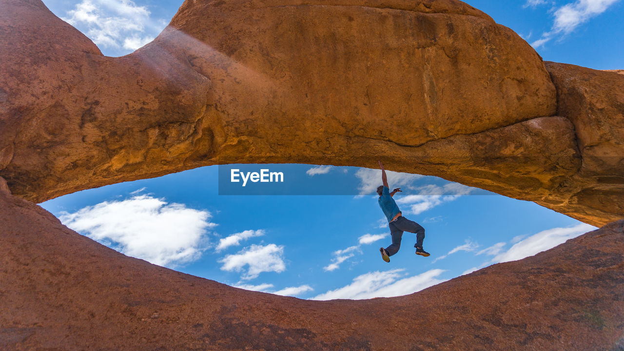 Low angle view of man jumping on rock against sky