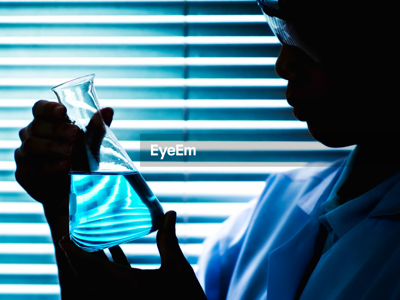 Close-up of female scientist holding chemical in conical flask in laboratory