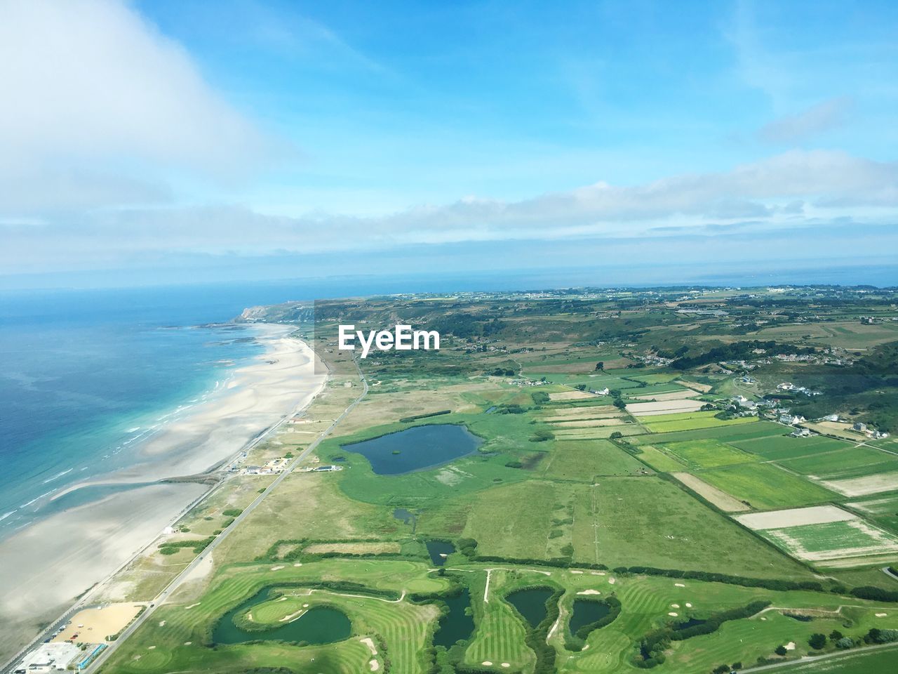 Aerial view of field and sea against blue sky