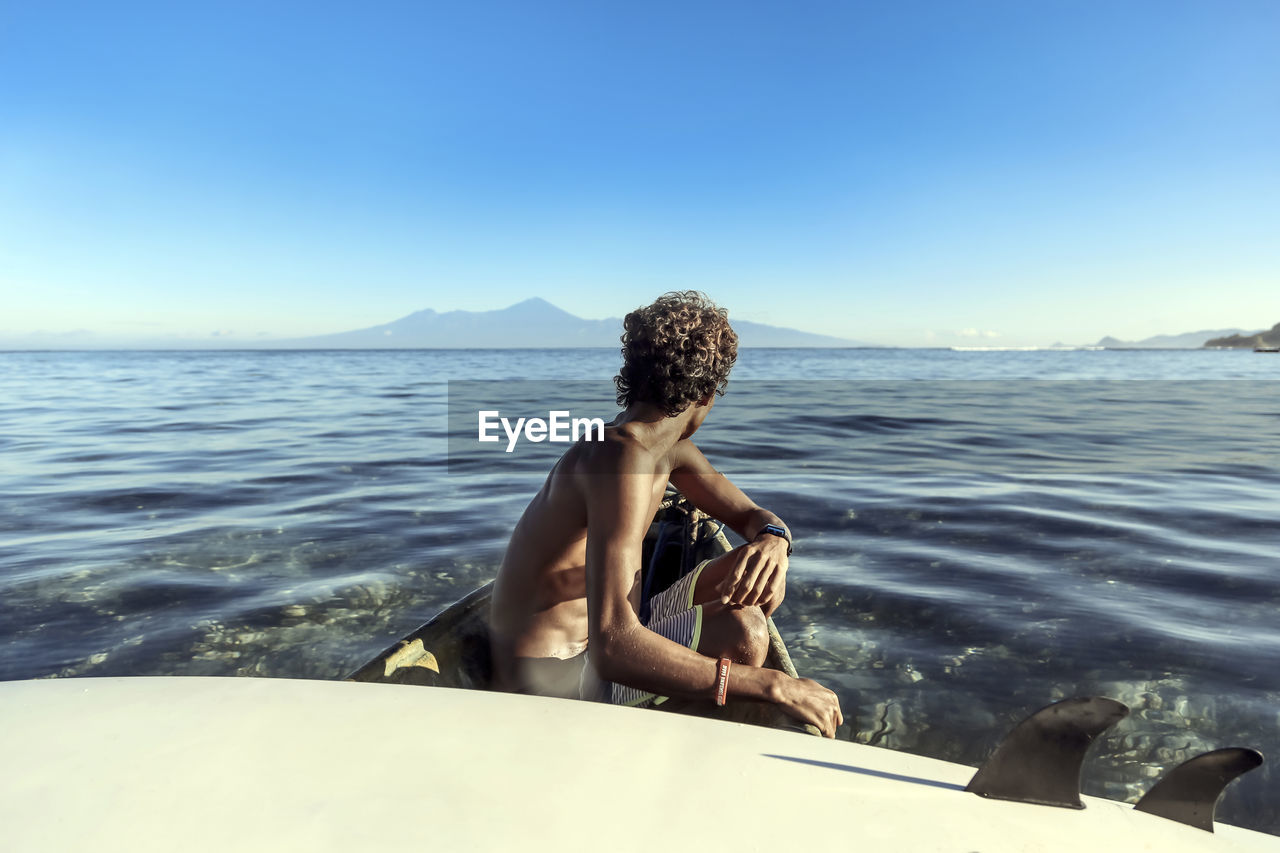 Side view of anonymous man with surfboard sitting in rowboat