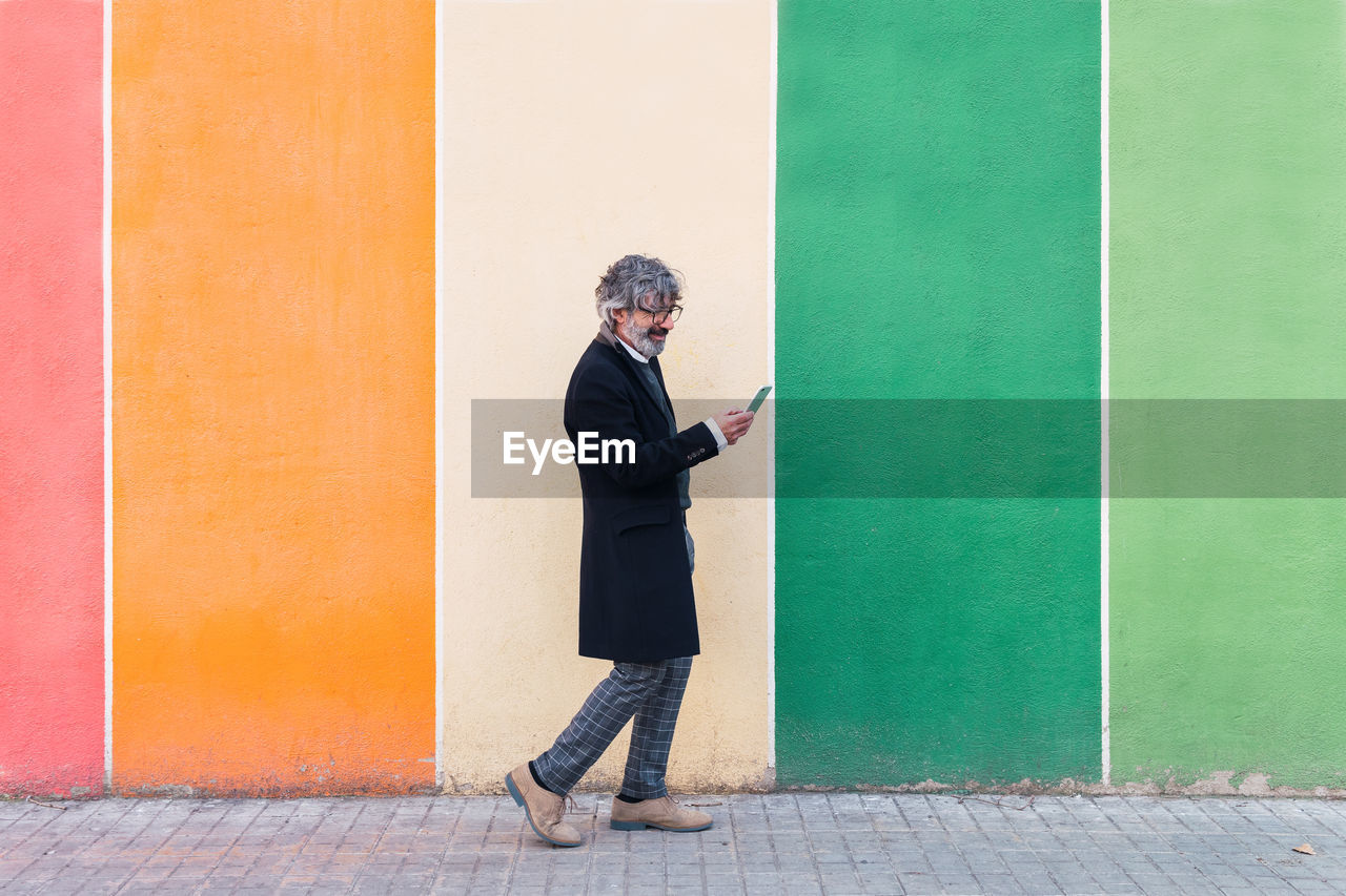 Mature businessman using mobile phone near color palette wall. colorful background