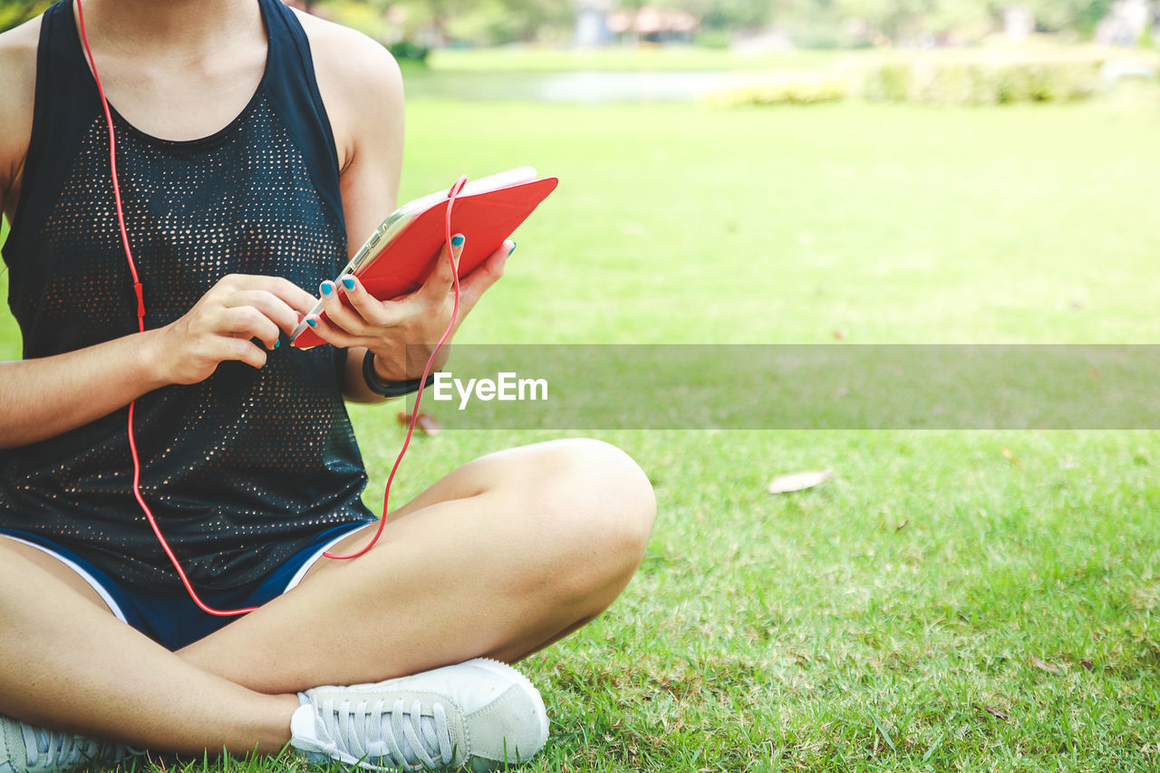 low section of woman using mobile phone while sitting on grass