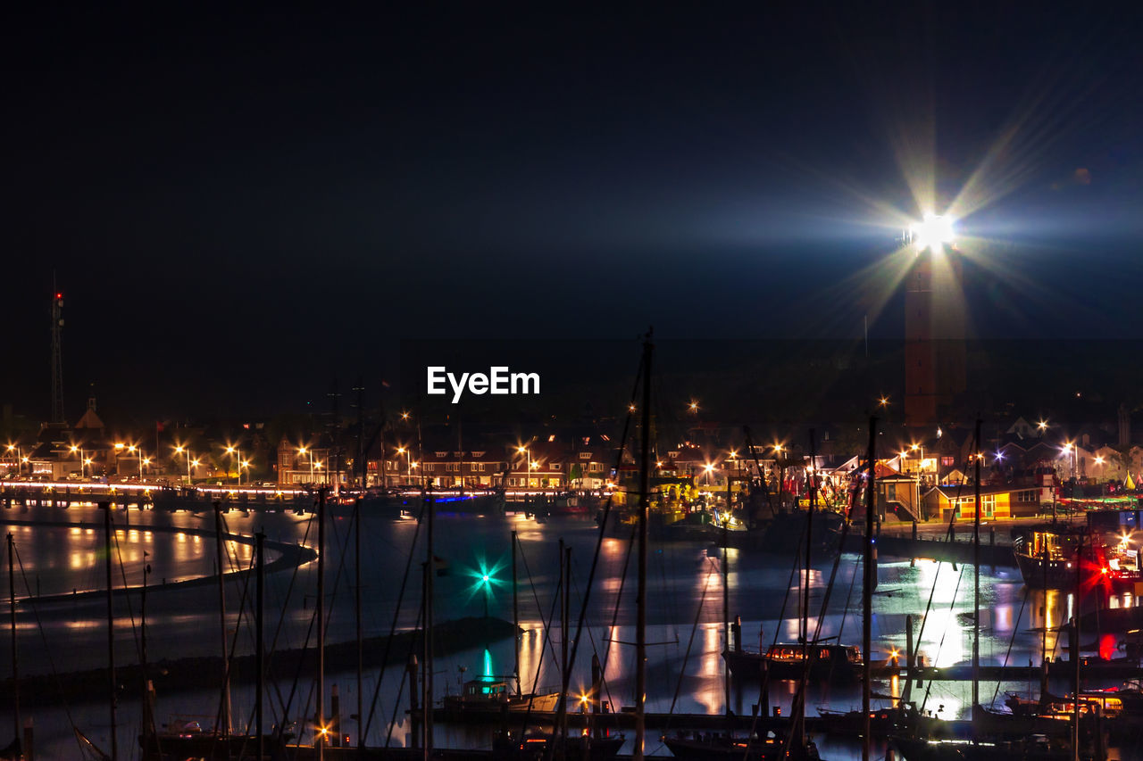 Illuminated buildings by river against sky at night