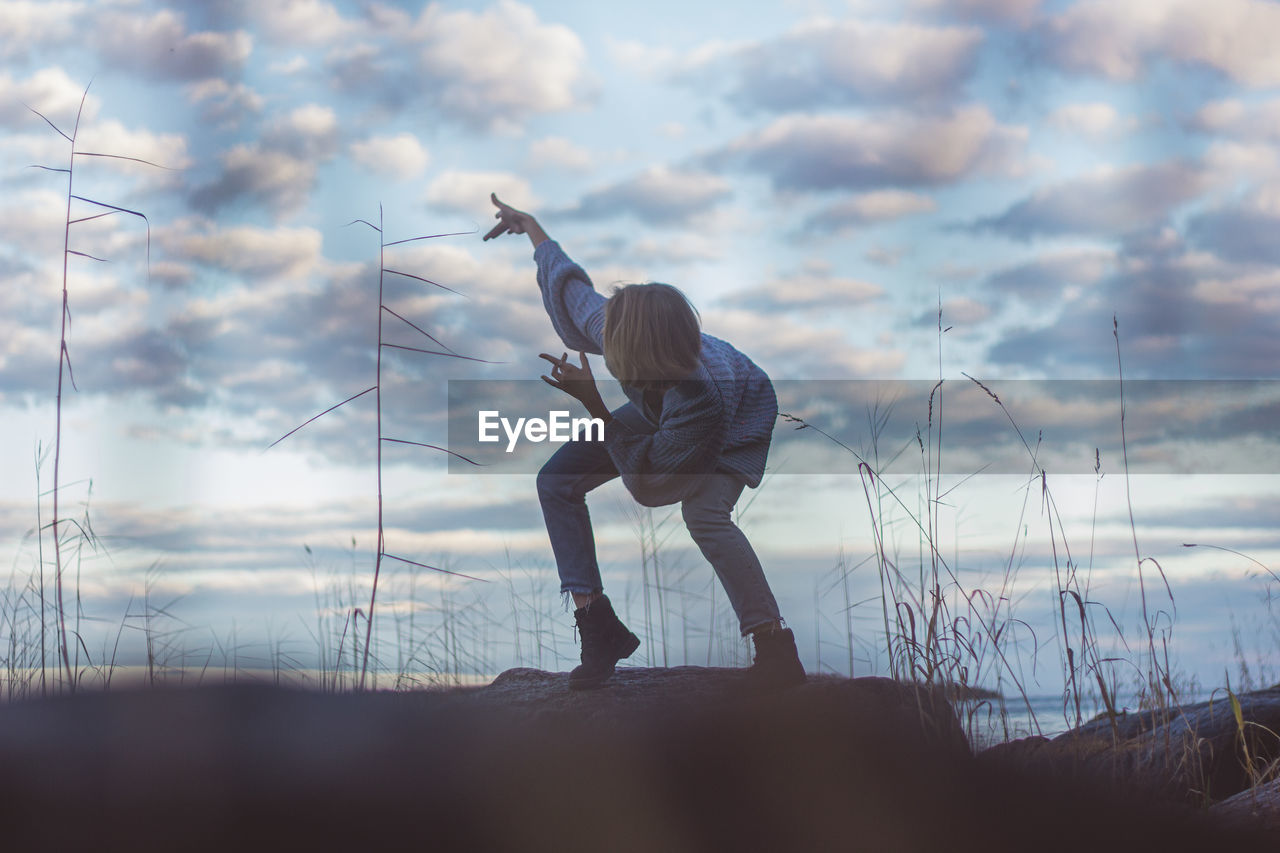 Young woman dancing on rock against cloudy sky