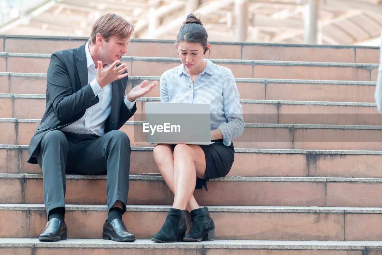 FULL LENGTH OF MAN USING MOBILE PHONE WHILE SITTING IN OFFICE