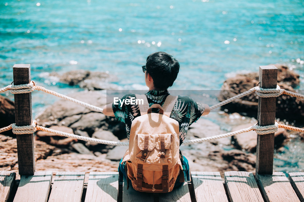 REAR VIEW OF MAN LOOKING AT SEA AGAINST RAILING