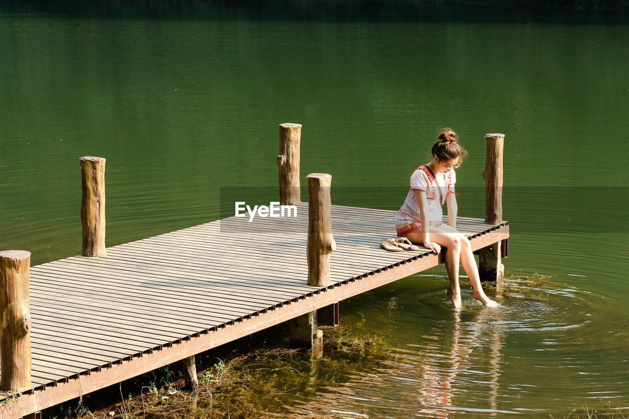 FULL LENGTH OF WOMAN SITTING ON PIER OVER LAKE