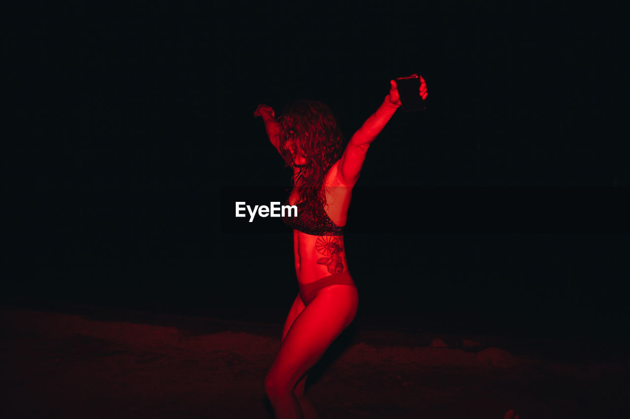 Group of young women having fun at a lakeside party at night with a red light