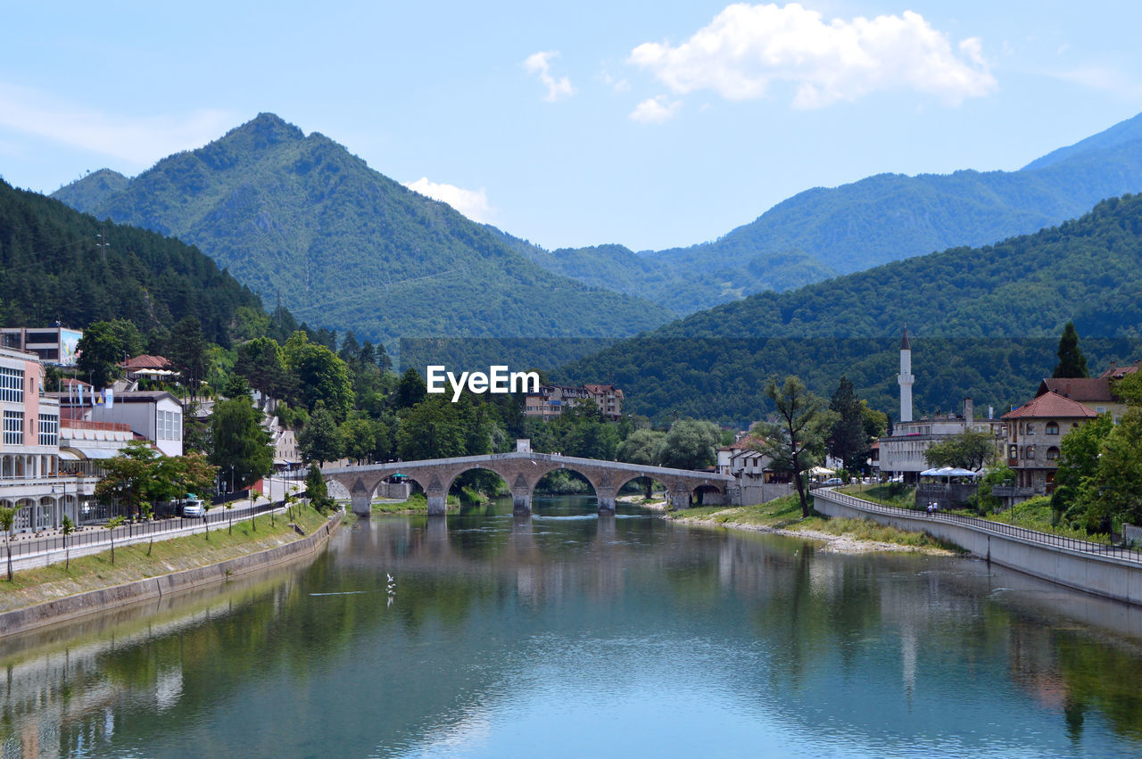 Arch bridge over river by buildings against sky