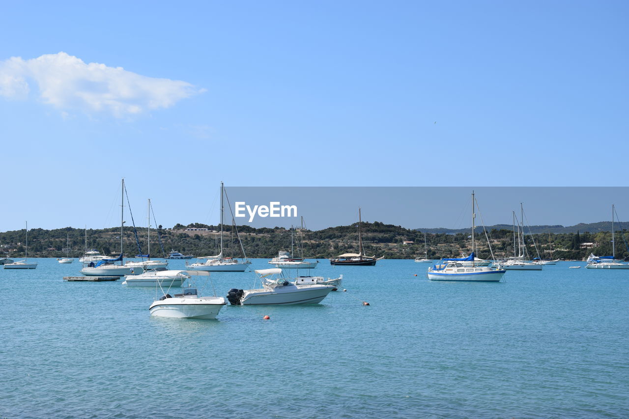 Sailboats moored on sea against blue sky