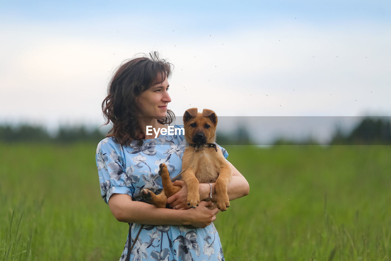 Young woman holding puppy on field against sky