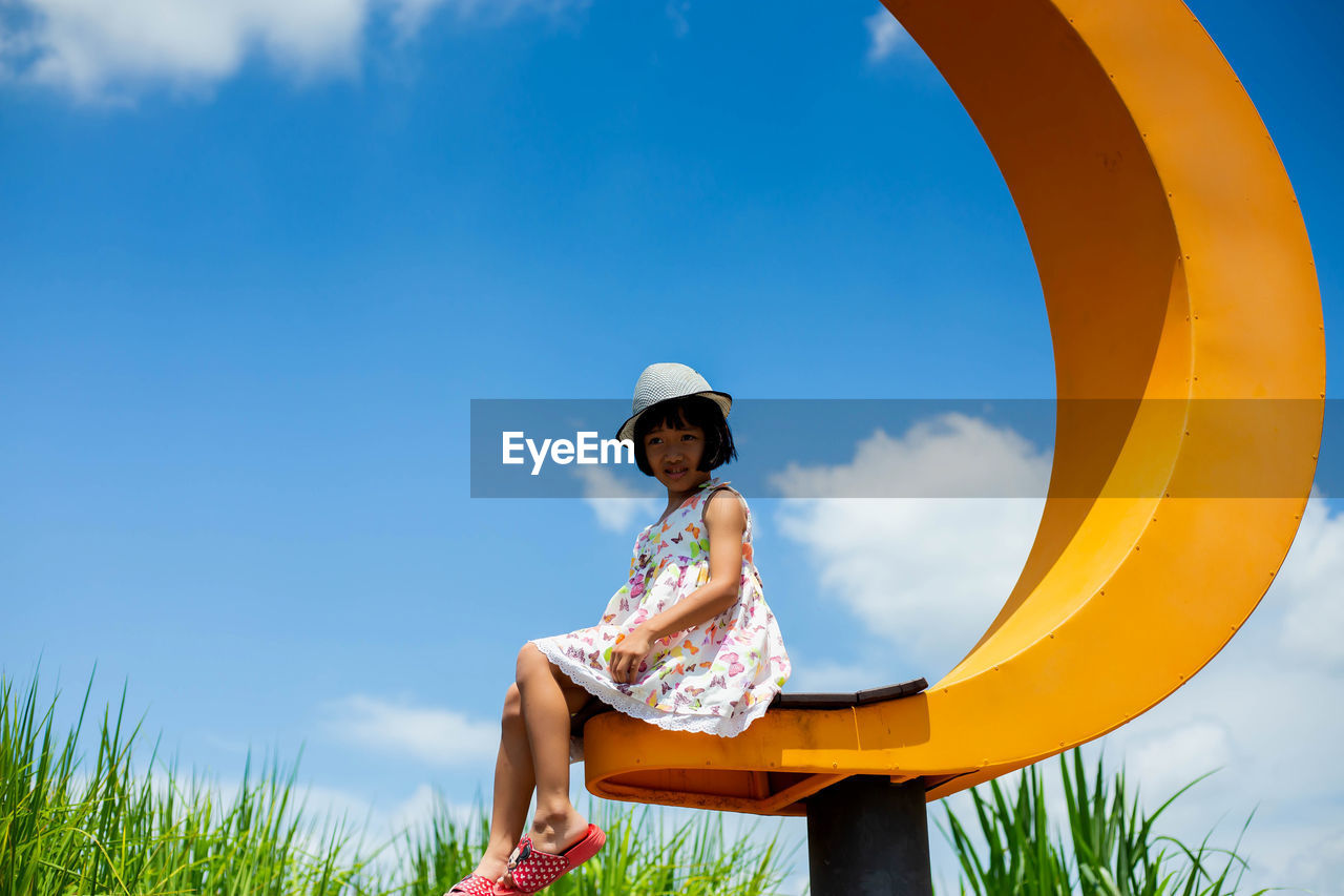 Low angle view of girl sitting on land against sky