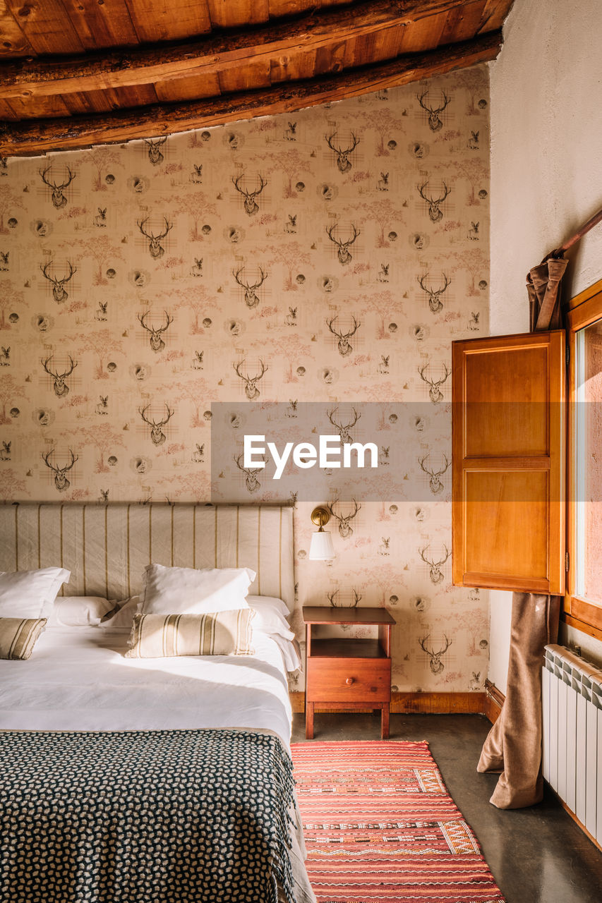 Interior of stylish bedroom with comfortable bed covered with coverlet near window decorated with curtains