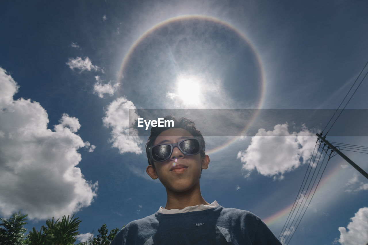 Low angle portrait of boy wearing sunglasses standing against sky during sunny day