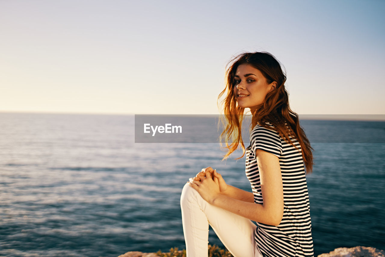 BEAUTIFUL YOUNG WOMAN SMILING AGAINST SEA AGAINST SKY