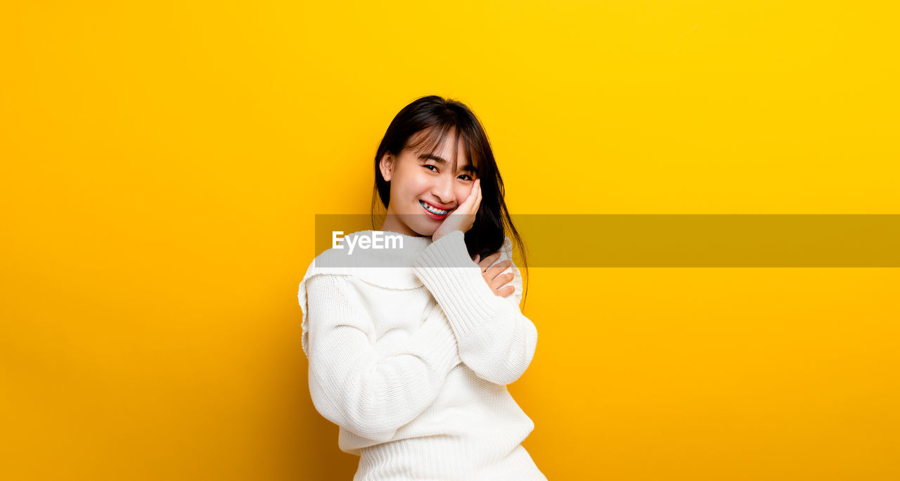 PORTRAIT OF HAPPY WOMAN STANDING AGAINST YELLOW BACKGROUND