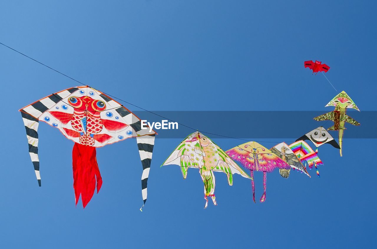 Low angle view of kites hanging against clear blue sky