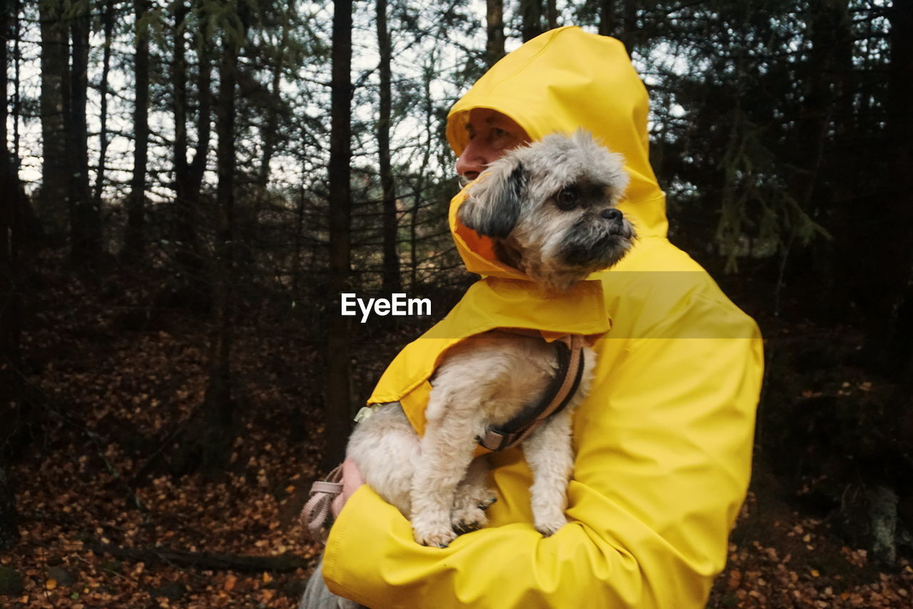 Man wearing yellow raincoat carrying dog in forest